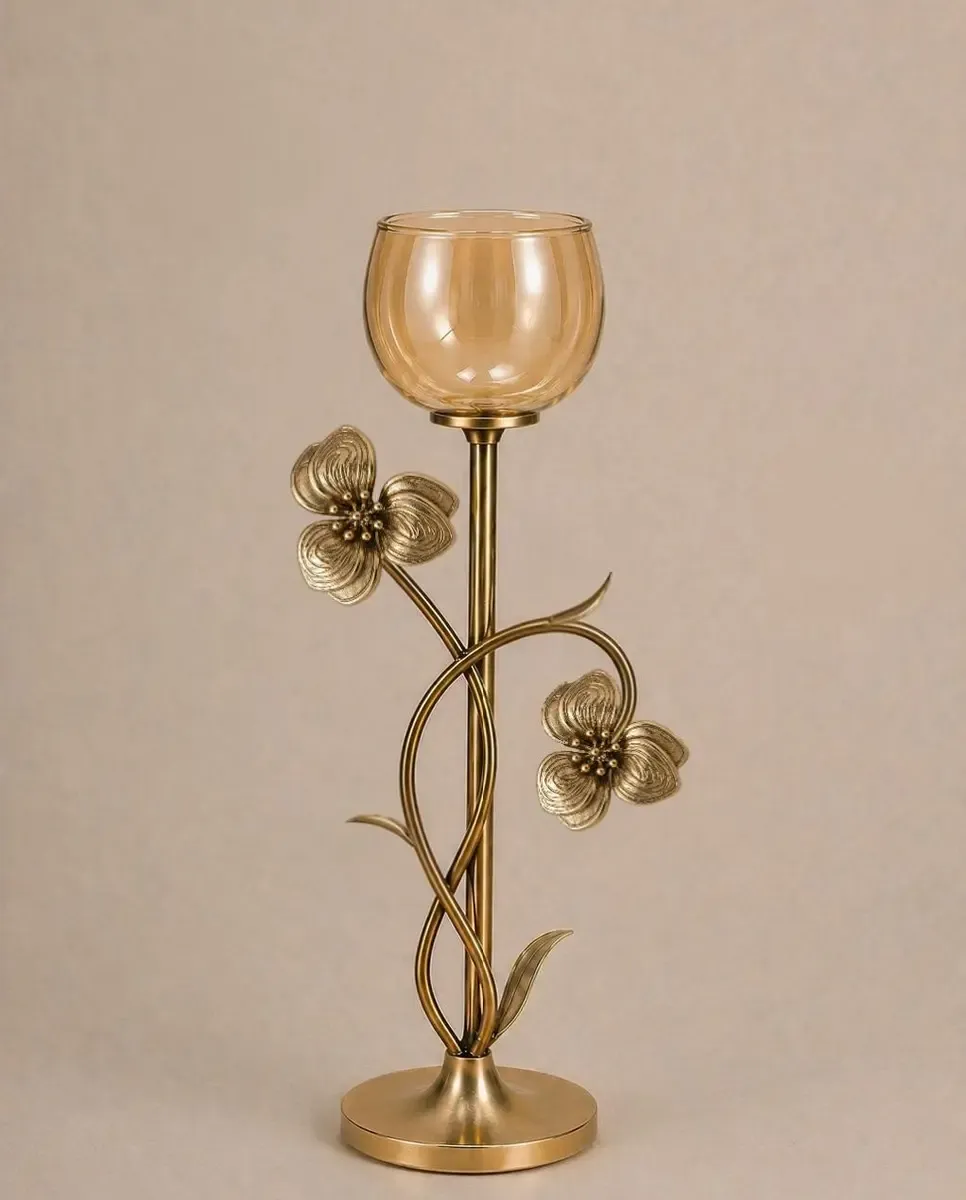 Stemmed candle holder in antique gold metal with an amber-tinted glass cup and two flowers on the stem