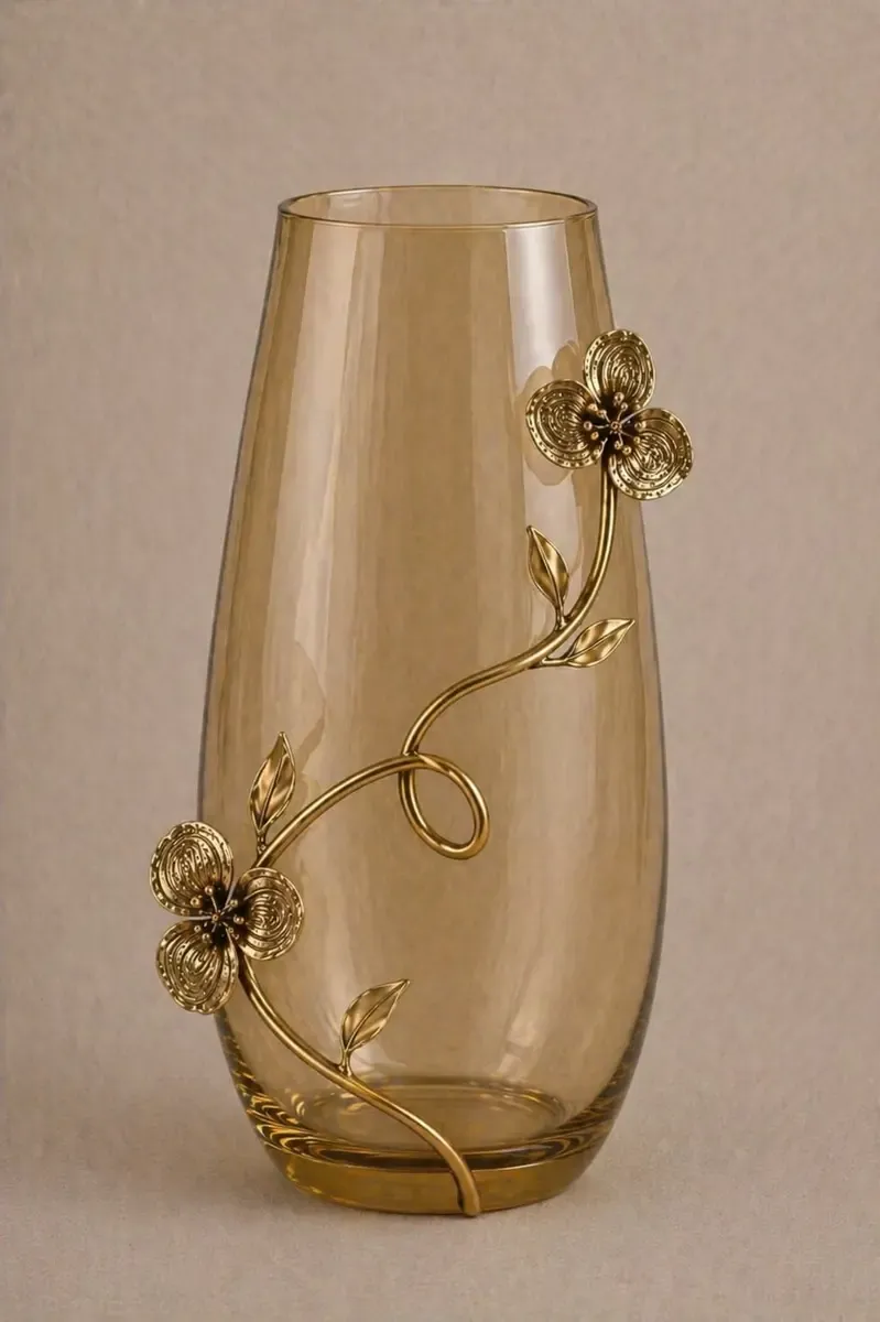 Decorative vase in amber-tinted glass wrapped by an antique gold metal flower and curling stem