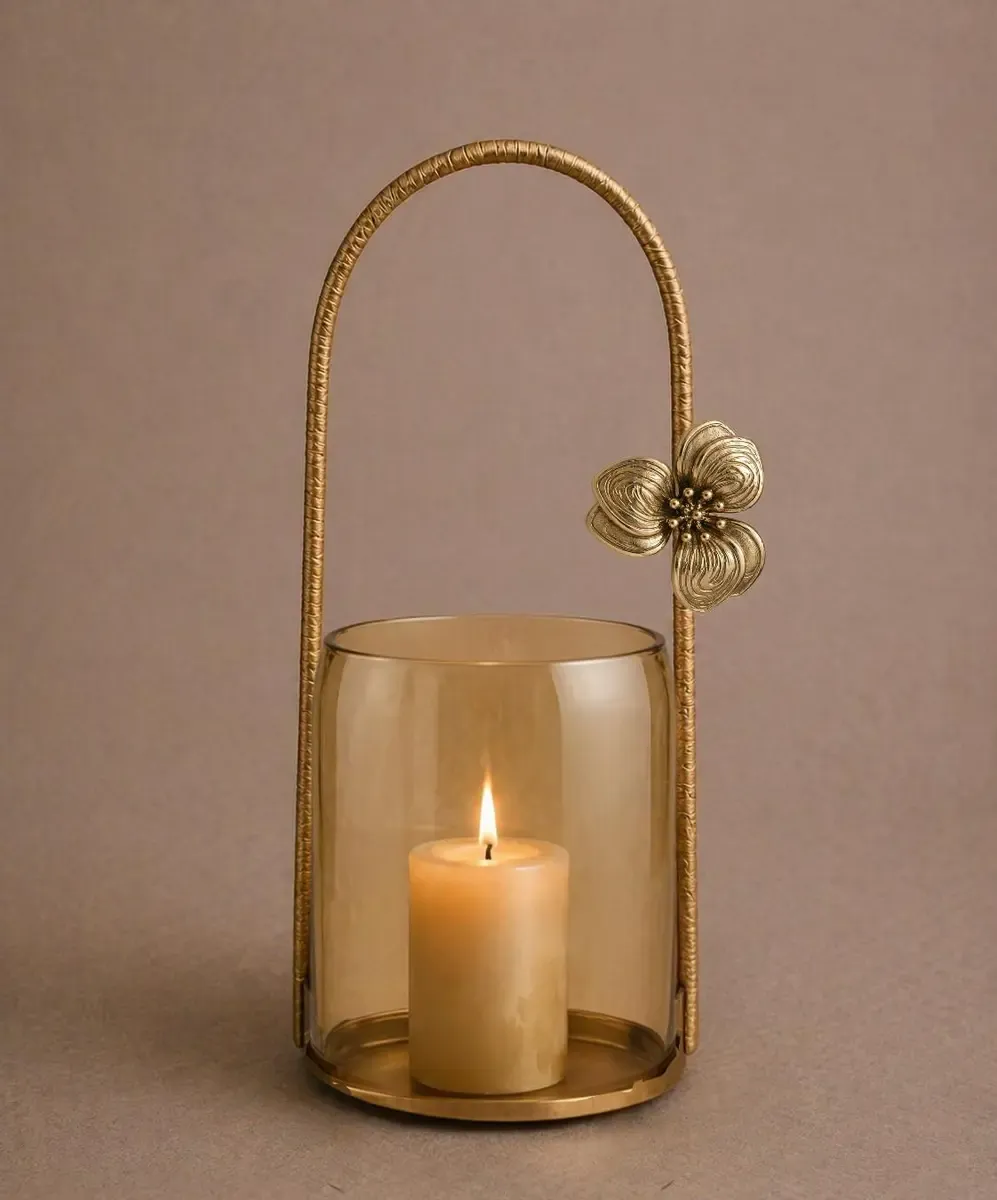 Hurricane lantern with an amber-tinted glass cylinder, a pillar candle and an arched antique gold metal handle with a flower
